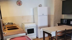 Une cuisine compacte équipée d’une cuisinière, d’un four, d’un réfrigérateur et d’un four à micro-ondes. On peut également apercevoir un évier avec un robinet et une table avec des chaises.
