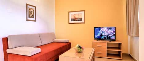 Een woonkamer met een rode bank, een salontafel, een televisie op een houten dressoir en twee ingelijste foto's aan de muur.