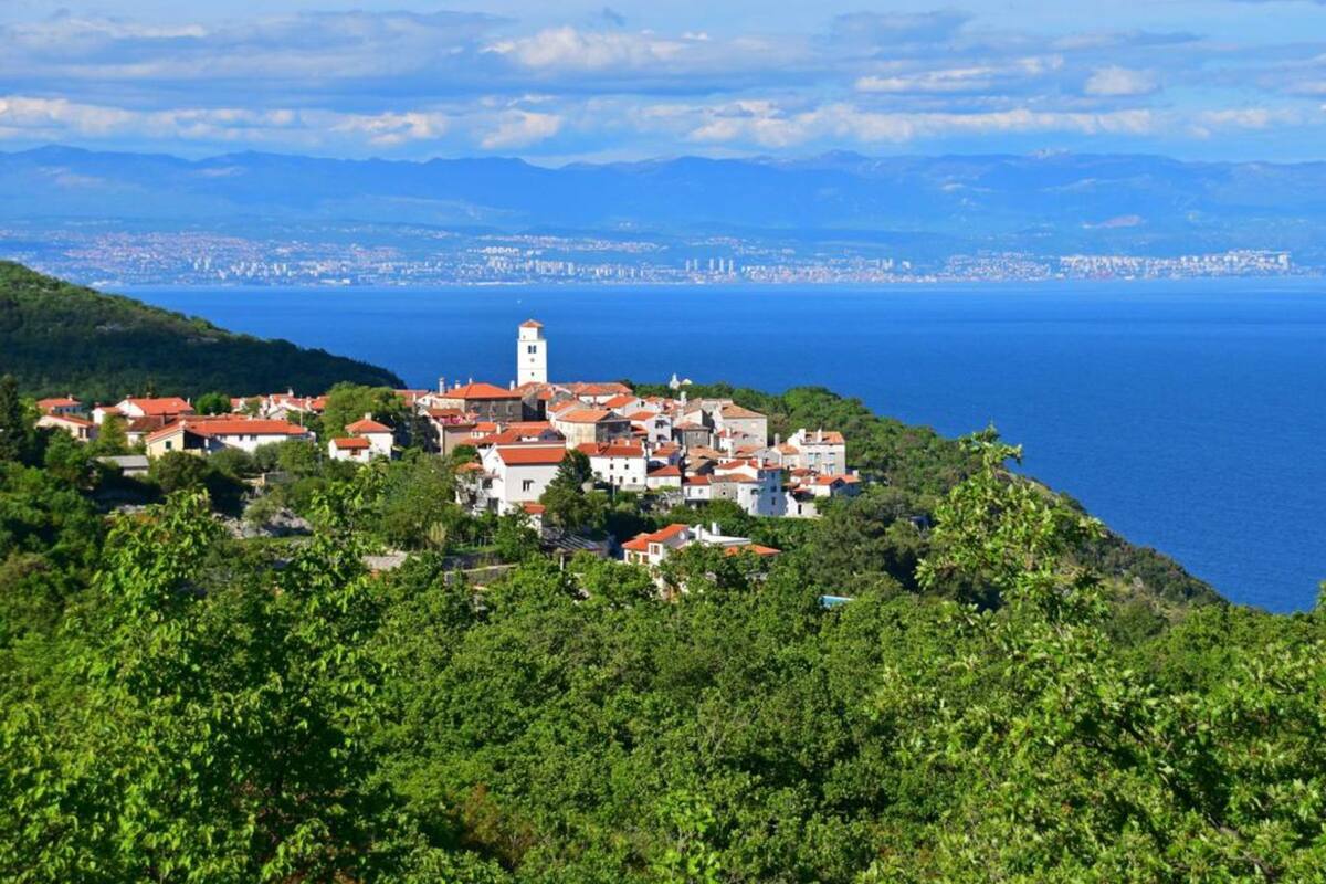 A coastal village with a prominent tower, surrounded by lush greenery and overlooking the sea.