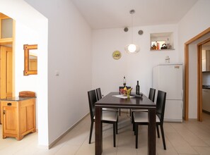 Un coin repas avec une table en bois, des chaises noires, un panier de fruits et une horloge au mur.