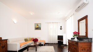 Ein Wohnzimmer mit einem weißen Sofa, einer Holzkommode, einem Fernseher und einem Bild an der Wand.