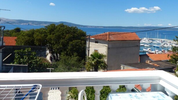 Vista sulla costa con un porto turistico, edifici dai tetti in tegole rosse e cielo sereno.