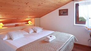 A neatly made bed with white linens, a wooden ceiling, and a window with curtains. - Sunny Holiday Home With Terrace (Lovran)