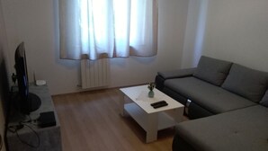 Una sala de estar moderna con un sofá gris, una mesa de centro blanca y un televisor de pantalla plana sobre un soporte.