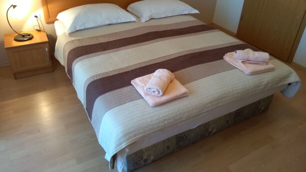 Una cama bien tendida con ropa de cama a rayas, dos almohadas y toallas dobladas en la cabecera.