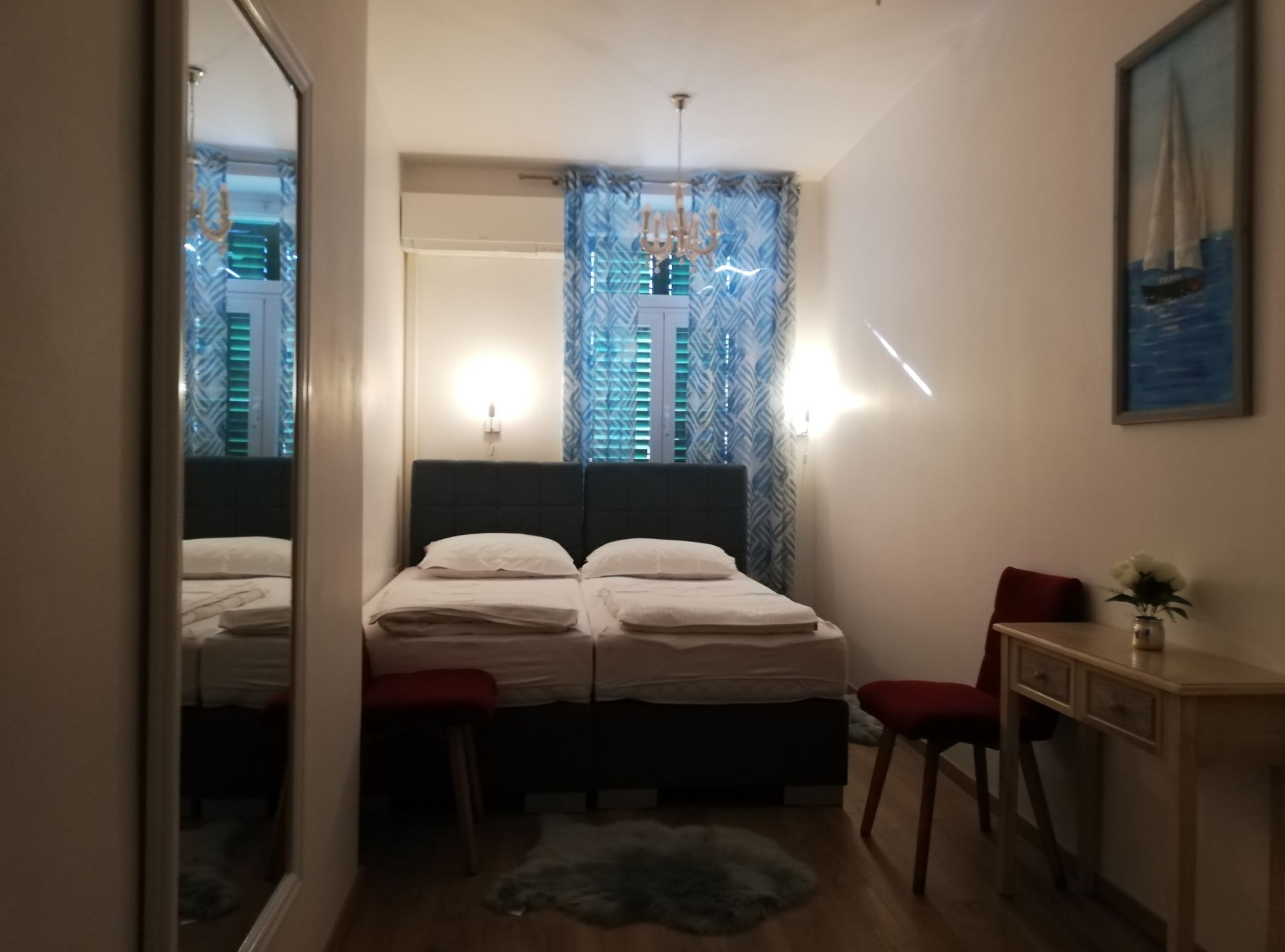 Une chambre à coucher comprenant un lit, des tables de chevet, une chaise, un bureau, un miroir et une fenêtre avec des rideaux.