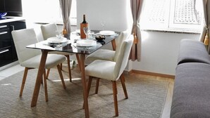 Un coin repas avec une table en verre, des chaises blanches et une bouteille de vin.