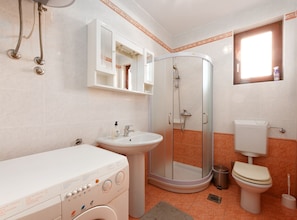 A bathroom with a washing machine, sink, toilet, and a glass shower enclosure.
