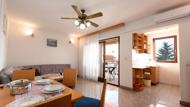 A dining area with a table set for four, a ceiling fan, a sofa, and a view of the outside through a glass door. - Cozy Icici Apartment With Sea View (Opatija)