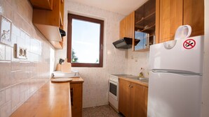 A compact kitchen with wooden cabinets, a built-in oven, a refrigerator, and a window providing natural light. - Cozy Icici Apartment With Sea View (Opatija)