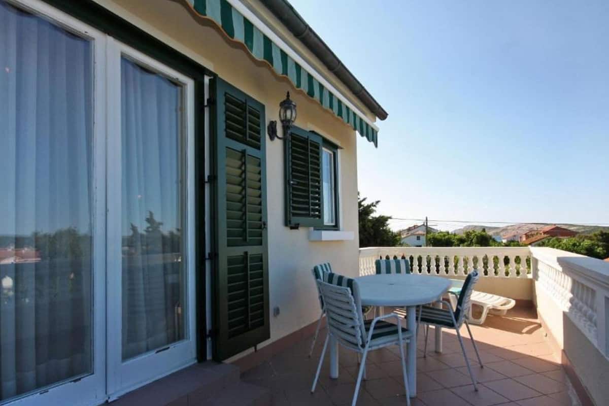 A balcony with a table and chairs, a sliding glass door, and a view of the surrounding landscape.