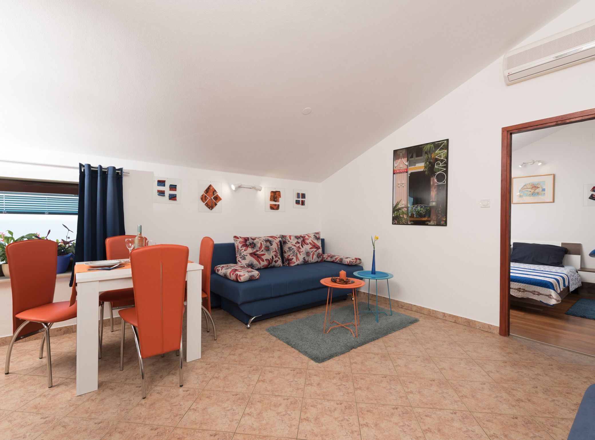 Un salon moderne avec un canapé bleu, des fauteuils orange, une table à manger et une petite table d’appoint.