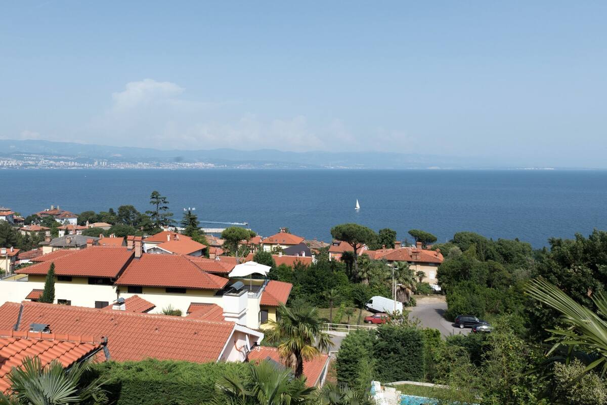A coastal residential area with red-tiled roofs, a clear view of the sea, and a distant lighthouse.