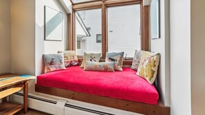 Een slaapkamer met dakraam, een rood bedlaken en meerdere decoratieve kussens.