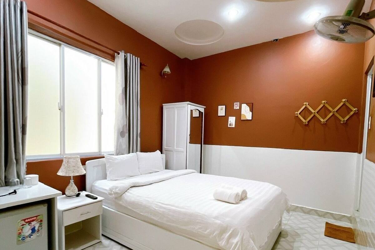 A hotel room with a bed, a nightstand, a lamp, a wardrobe, and a window with curtains.
