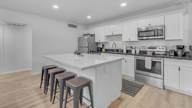 A modern kitchen with white cabinets, a large island with stools, stainless steel appliances, and a herringbone tile backsplash. - Splash Pad - Toys - Pets OK - 8 Min to Oldtown (Scottsdale)