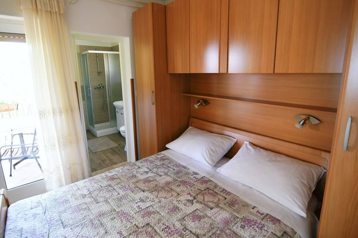 Una camera da letto con un letto, un armadio in legno e un bagno visibile attraverso una porta aperta.