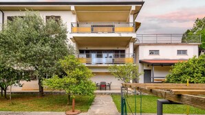 A two-story residential building with a balcony, a stone pathway leading to the entrance, and a small garden area. - Charming Lovran Apartments With Wonderful Sea View (Lovran)