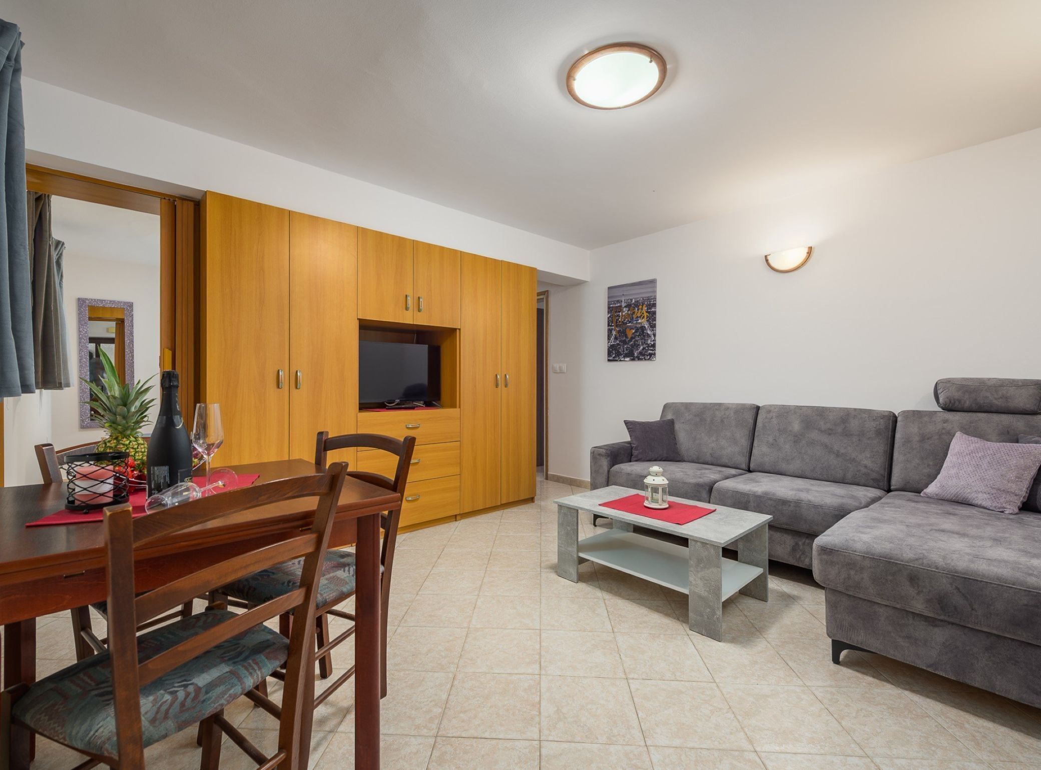 A modern living room with a grey sofa, wooden dining table, and a TV on a wooden cabinet.