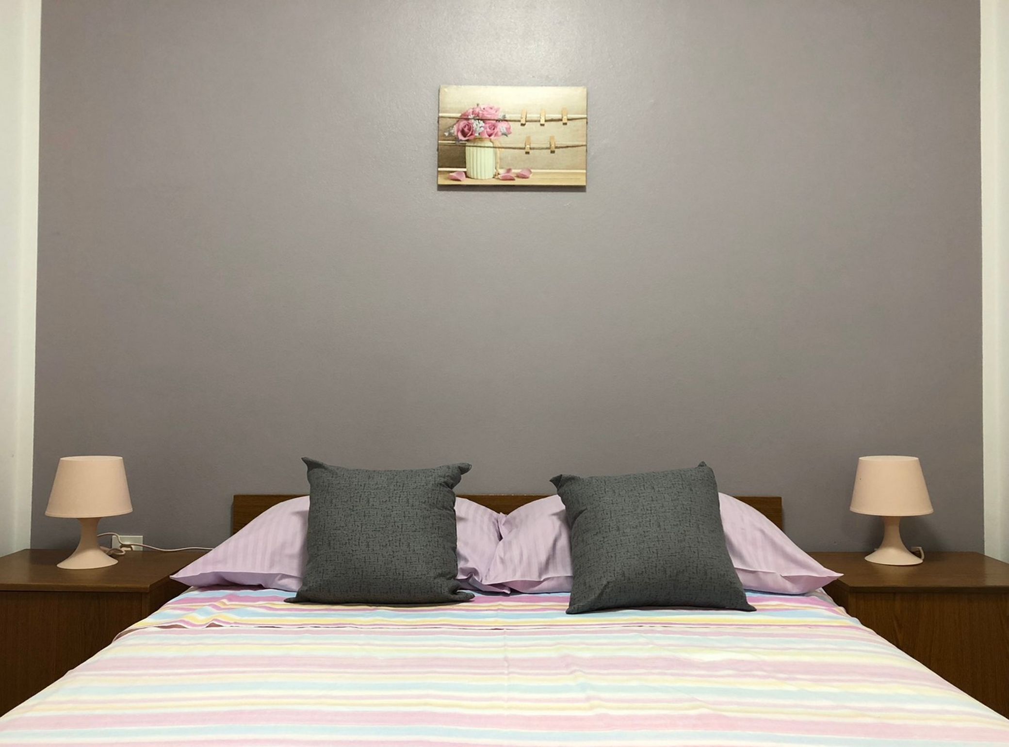 Ein Schlafzimmer mit einem Bett, zwei Kissen, einem Nachttisch mit Lampe und einem Wandbild.