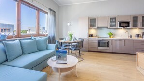 Uma sala de estar moderna com um sofá, uma mesa de centro e uma área de jantar. Há uma cozinha com armários e eletrodomésticos.