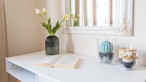 Uma escrivaninha branca com um livro aberto, um vaso de tulipas brancas e dois vasos de vidro decorativos com detalhes azuis e brancos.
