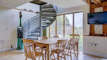 Un coin repas avec une table et des chaises en bois, un escalier en colimaçon, une pompe à essence verte et un téléviseur fixé à un mur en bois.