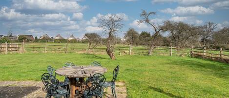 An outdoor patio with a round table and metal chairs, surrounded by a grassy area and a wooden fence.