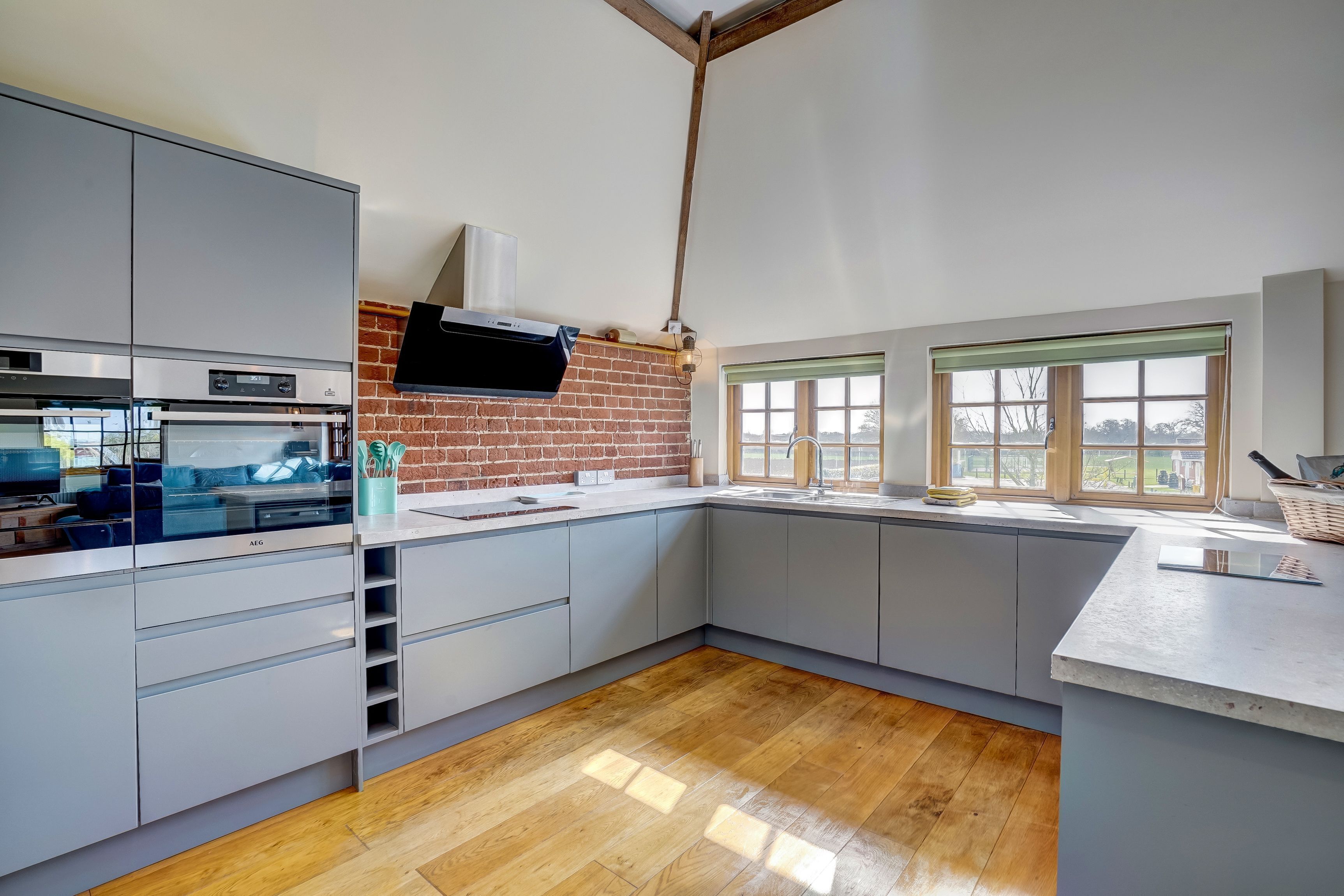 A modern kitchen with grey cabinets, a brick wall, and a large window.