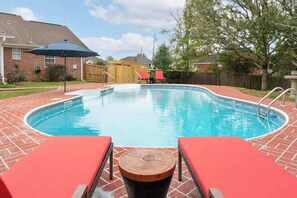 Ein rechteckiger Pool mit Ziegelumrandung, umgeben von einer Holzterrasse.