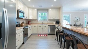 Une cuisine moderne avec des meubles blancs, des appareils en acier inoxydable, un comptoir-bar en bois et un tapis rouge.