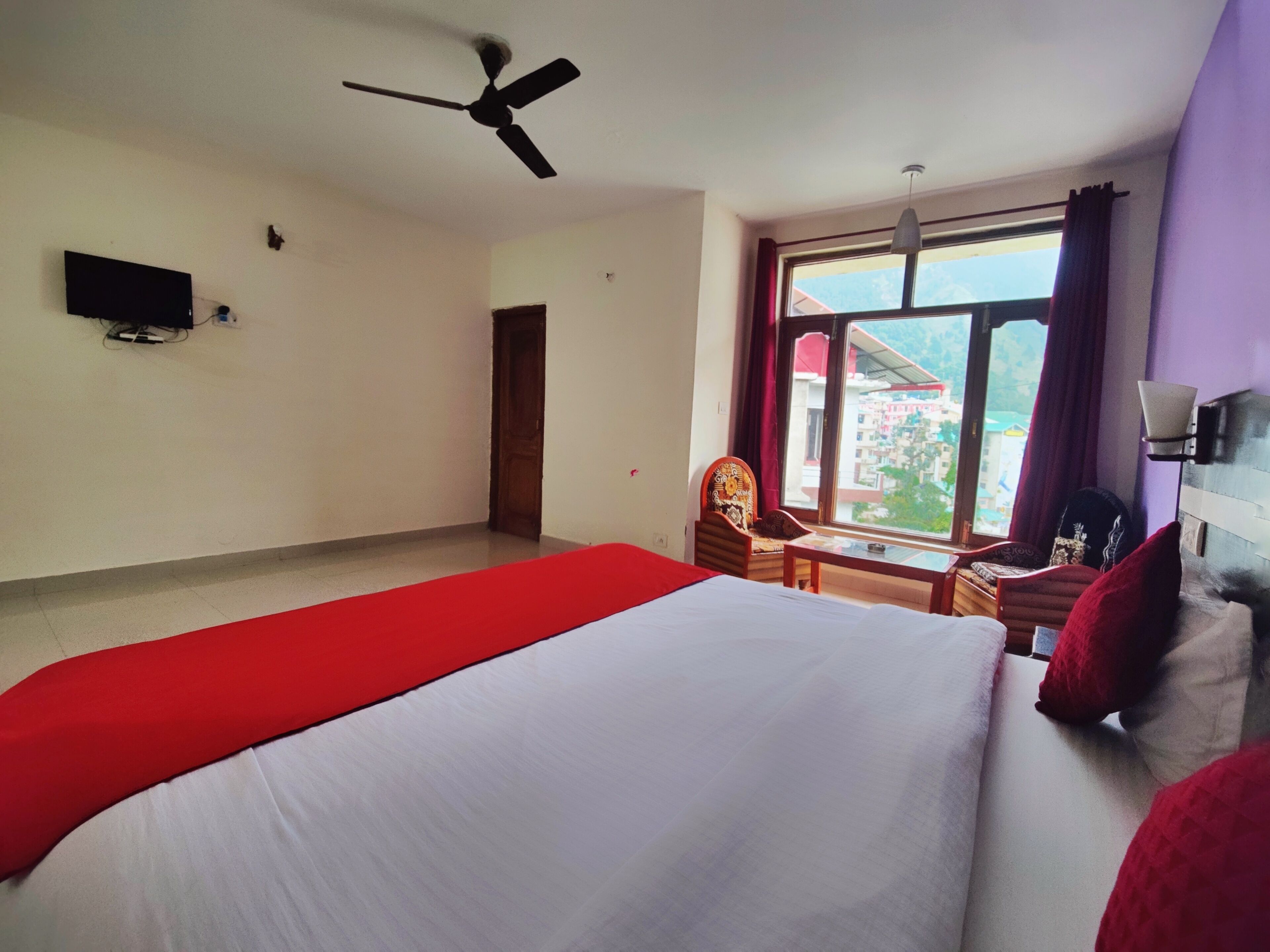 A hotel room with a bed, a desk, a chair, a television, and a window with a view of buildings.
