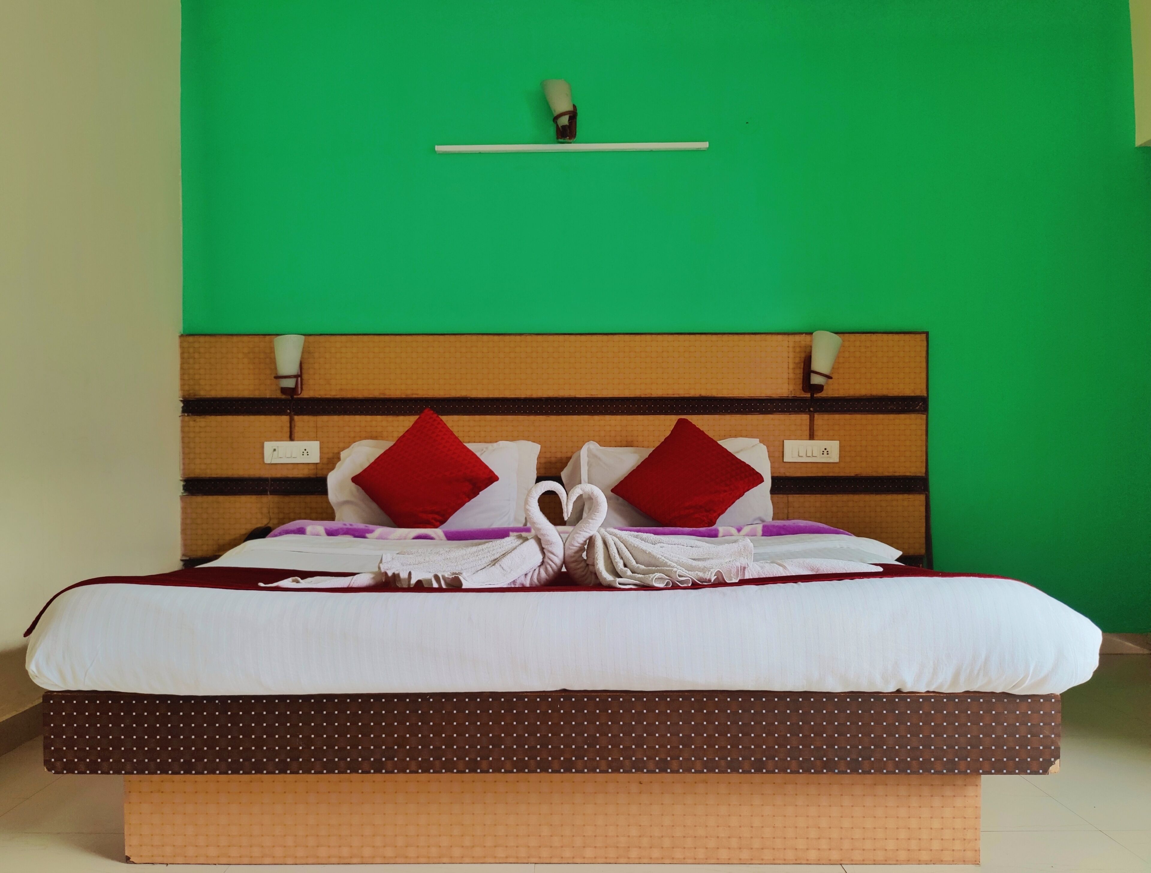 A bed with a wooden headboard, white bedding, red pillows, and a towel arrangement.