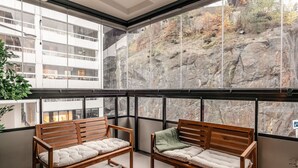 A balcony with two wooden benches, a table with a pitcher and glasses, and a view of a rocky hillside. - Stylish Waterfront Apt Stockholm (Stockholms län)