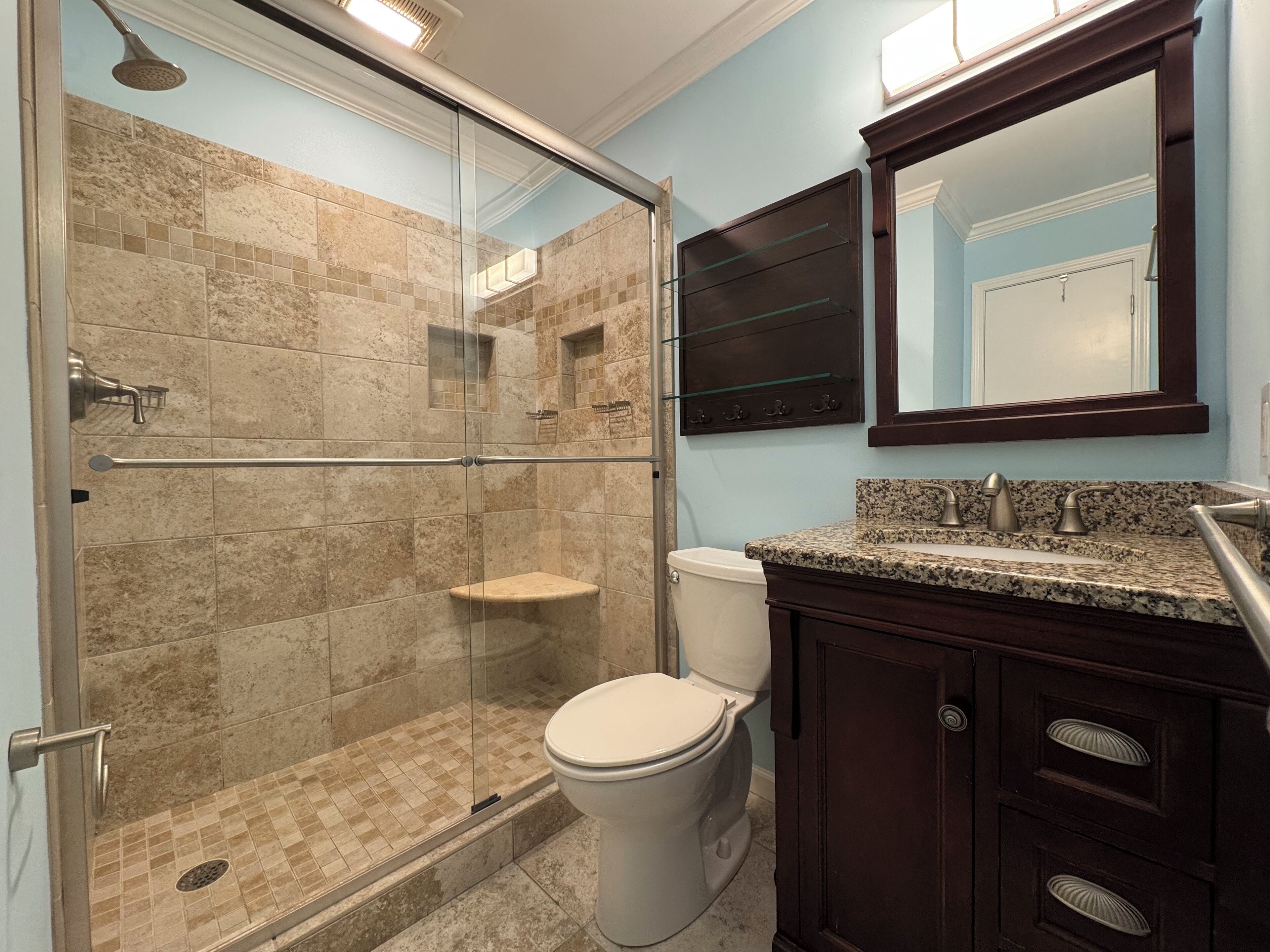 Un baño con ducha envuelta en vidrio, inodoro blanco y muebles de madera oscura.