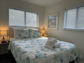 A bedroom with a bed, two bedside lamps, a framed picture on the wall, and a window with blinds. - Ocean View - Ocean Villas B201-Ocean View - Professionally Managed by HHB&T Vacation Rentals<br>STR Permit# 35350 (Hilton Head Island)