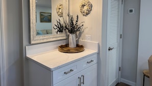 A bathroom vanity with a marble countertop, a large mirror, and decorative wall art. - Resort View - Tennis Villas A12-Professionally Managed by HHIB&T Vacation Rentals (Hilton Head Island)