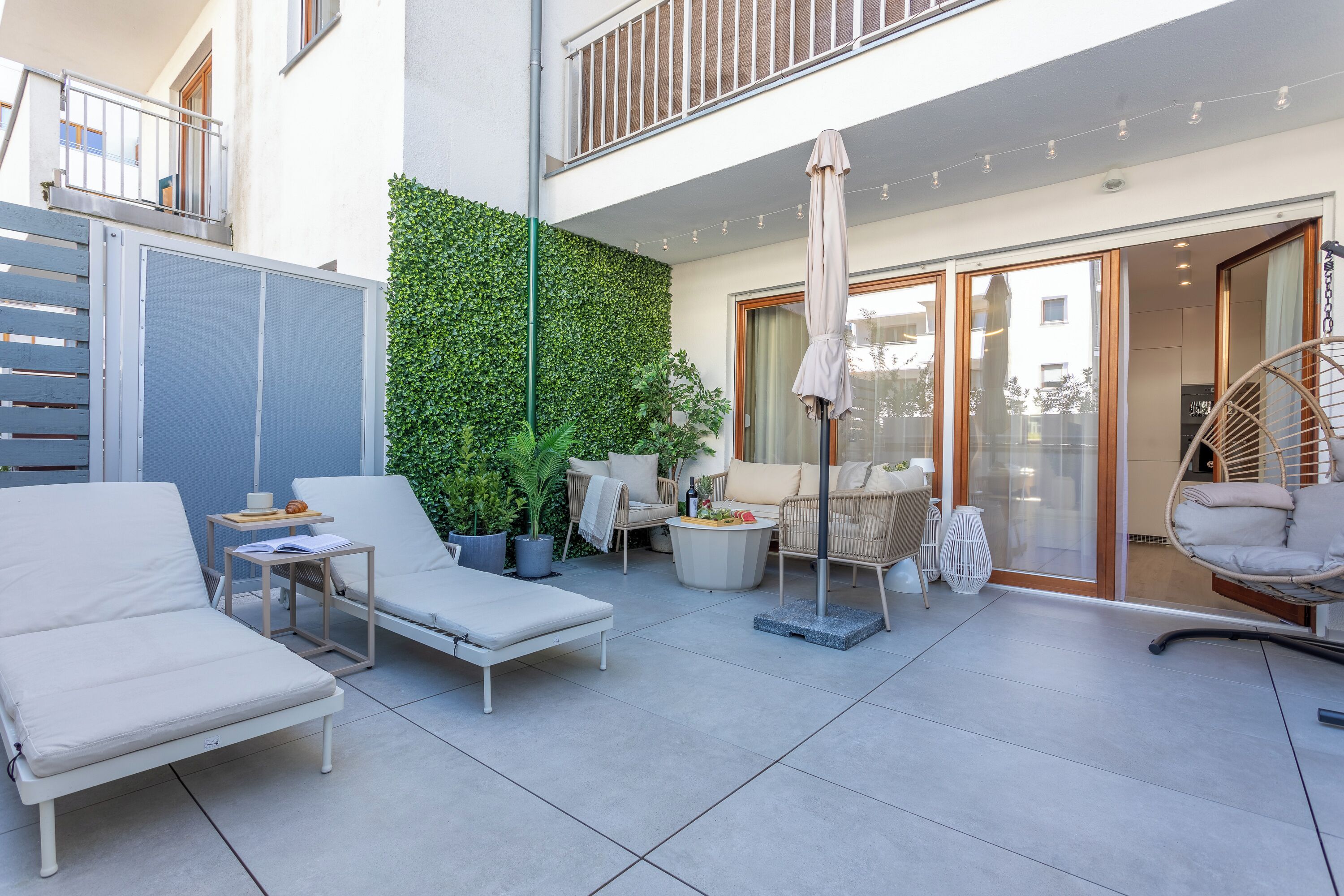 A modern outdoor patio with lounge chairs, a small table, and a decorative plant wall.