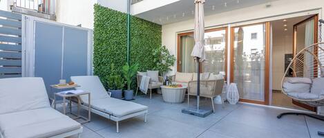 A modern outdoor patio with lounge chairs, a small table, and a decorative plant wall.