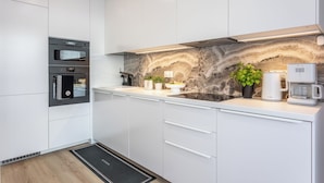 A modern kitchen with white cabinetry, a built-in oven, a marble backsplash, and a coffee maker. - Vacation apartment by the sea, vacation on the island of Usedom, Apartment White Space II (Swinoujscie)