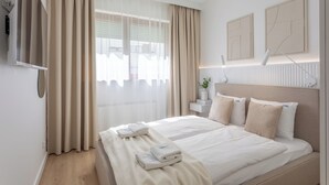 A hotel room with a bed, curtains, a TV, a bedside table with a lamp, and artwork on the wall. - Vacation apartment by the sea, vacation on the island of Usedom, Apartment White Space II (Swinoujscie)