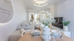 A modern living room with a dining area, featuring a round wooden table set for two, a white vase with flowers, and a flat-screen TV mounted on the wall. - Vacation apartment by the sea, vacation on the island of Usedom, Apartment White Space II (Swinoujscie)