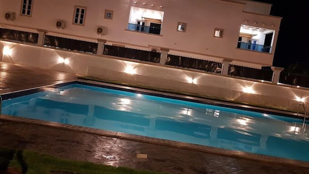 A rectangular swimming pool with a stone border, surrounded by a building with multiple windows and a balcony. - Porto Golf Hotels (Kano)