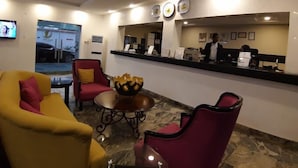 A reception area with a counter, chairs, a table with a decorative bowl, and a television mounted on the wall. - Porto Golf Hotels (Kano)