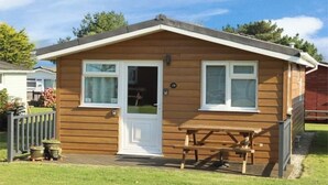 Une petite cabane en bois d’un seul étage, avec une porte d’entrée, deux fenêtres et une table de pique-nique.