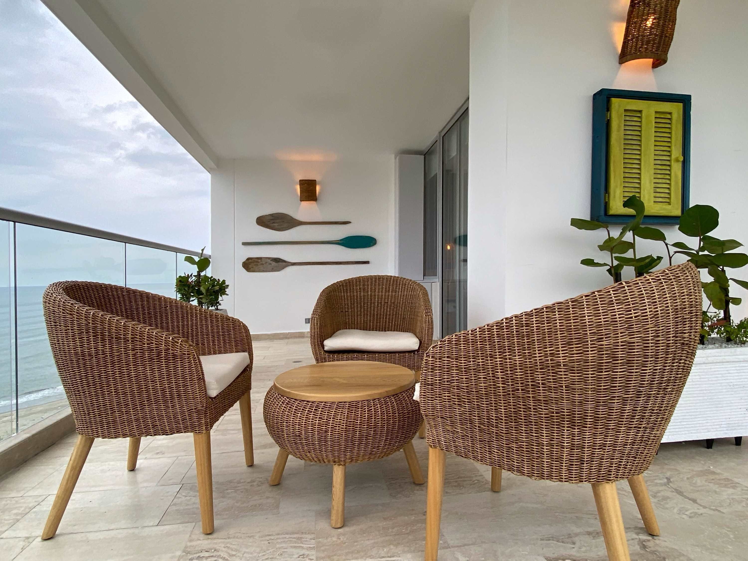 Ein Balkon mit Korbmöbeln, einem kleinen runden Tisch und Blick aufs Meer.