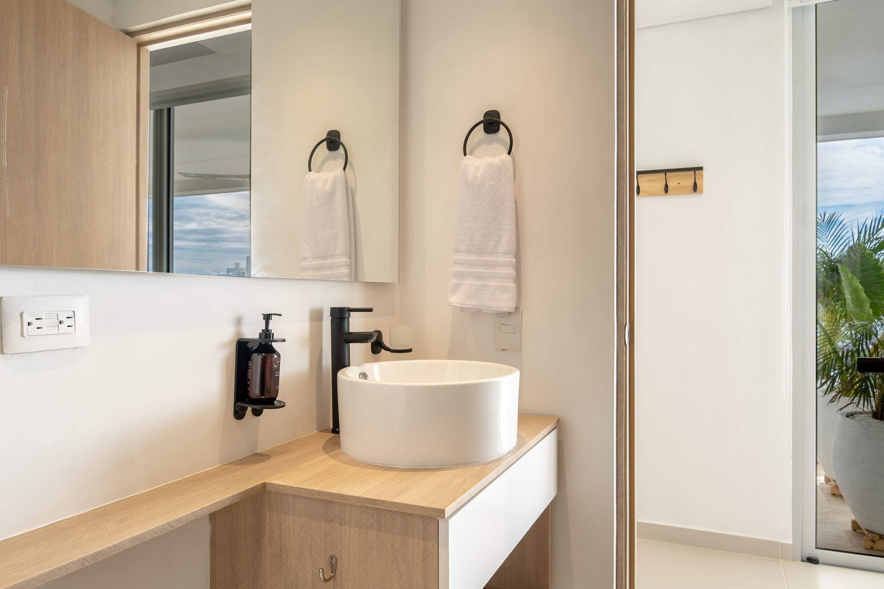 A modern bathroom with a white sink, black faucet, and a mirror above it. There are two towels hanging on hooks above the mirror.
