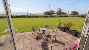 A patio with a table and chairs, a grassy lawn, and a view of the sea. - THE BOATHOUSE, family friendly in Carrigaholt, County Clare (Kilkee)