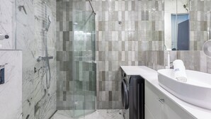 A modern bathroom with a glass-enclosed shower, a built-in washing machine, and a sink with a towel holder.