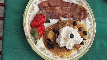 En tallerken med pandekager, blåbær, flødeskum og bacon på en tallerkend med blomstermønster.